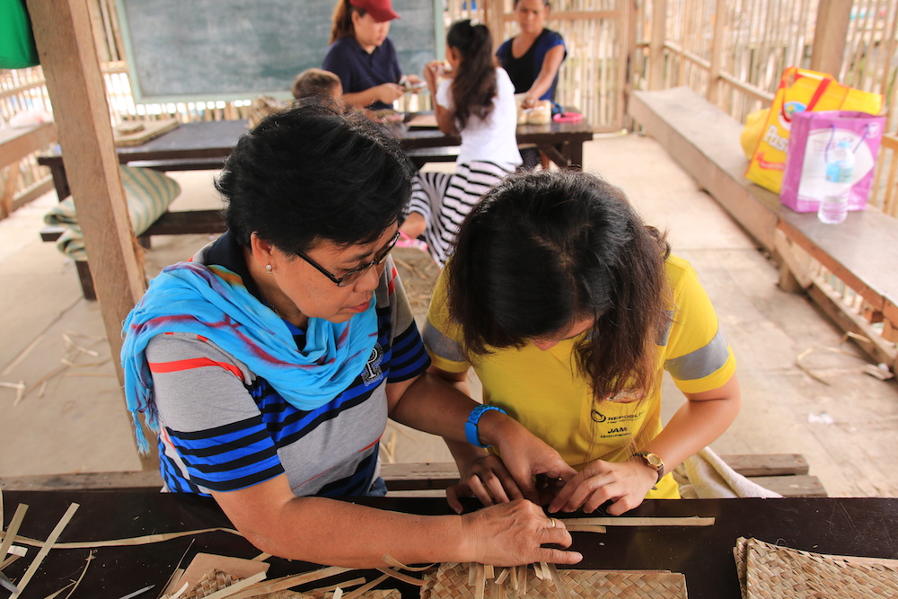 Republic Cement Community Relations Officer Jamaica Gonzales reviews the work quality of Bunawan Mat Weavers’ Association member, Primitiva Cuesta.