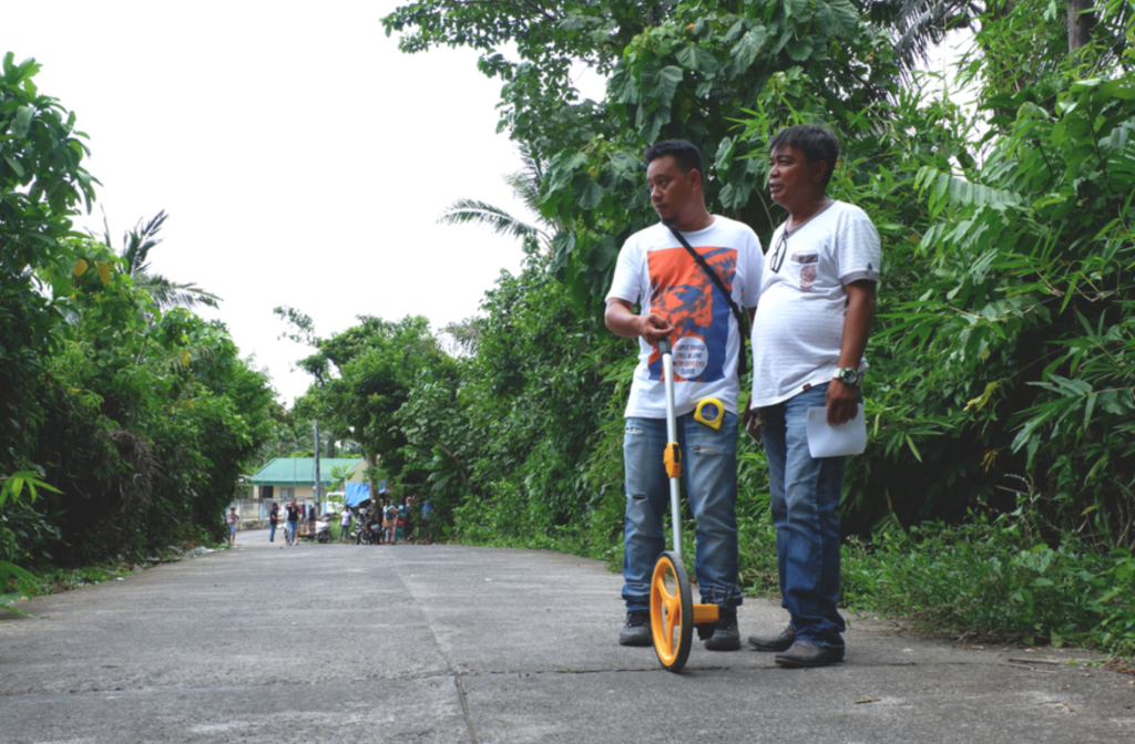 ROAD ACCESS IMPROVEMENT. Barangay Chairman Antonio Capa of Bagumbayan and Rey Clerigo of  Municipal Engineering Office measure the concrete road project funded through the ER 1-94 during the inspection conducted by APRI and DOE on May 16 to18 in Tiwi, Albay.
